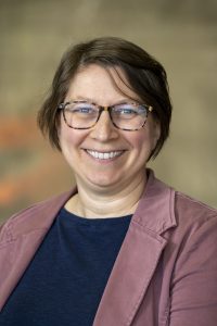 A headshot of Jennifer Headley wearing a mauve blazer and navy blouse. Jennifer has short brown hair and patterned framed glasses. 