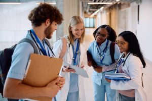 Multiracial group of happy medical students using touchpad in university hallway.