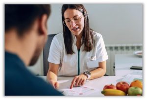 A nutritionist at a desk reading off a paper to a patient